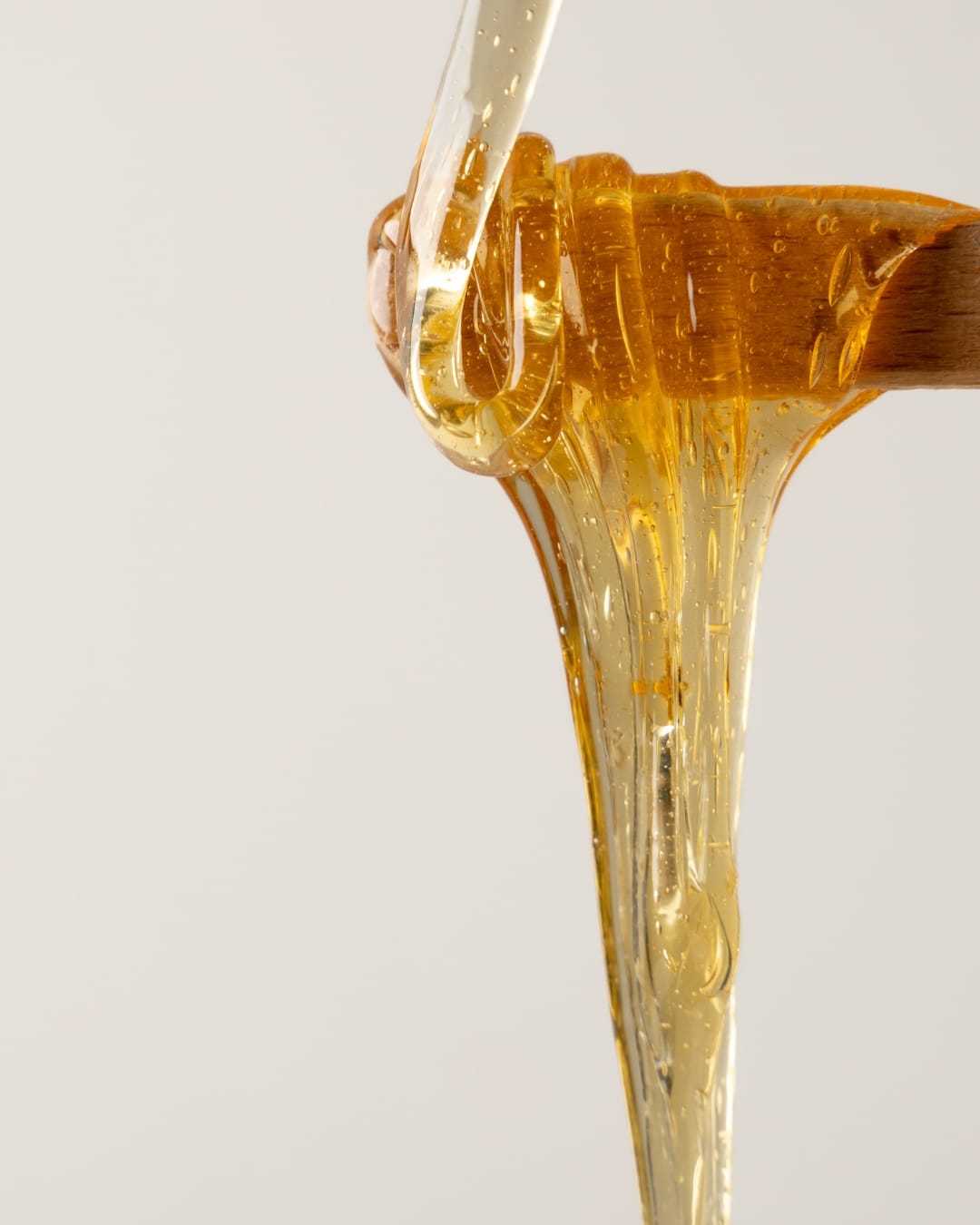 Honey dripping from a wooden dipper against a plain, light-colored background.