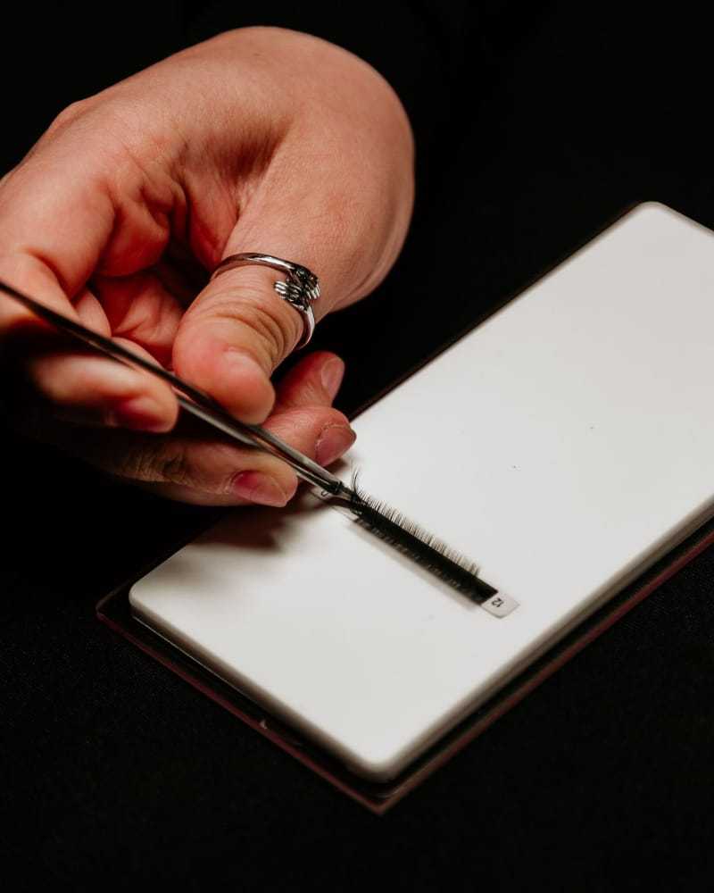 Applying false eyelashes with tweezers over a white surface.