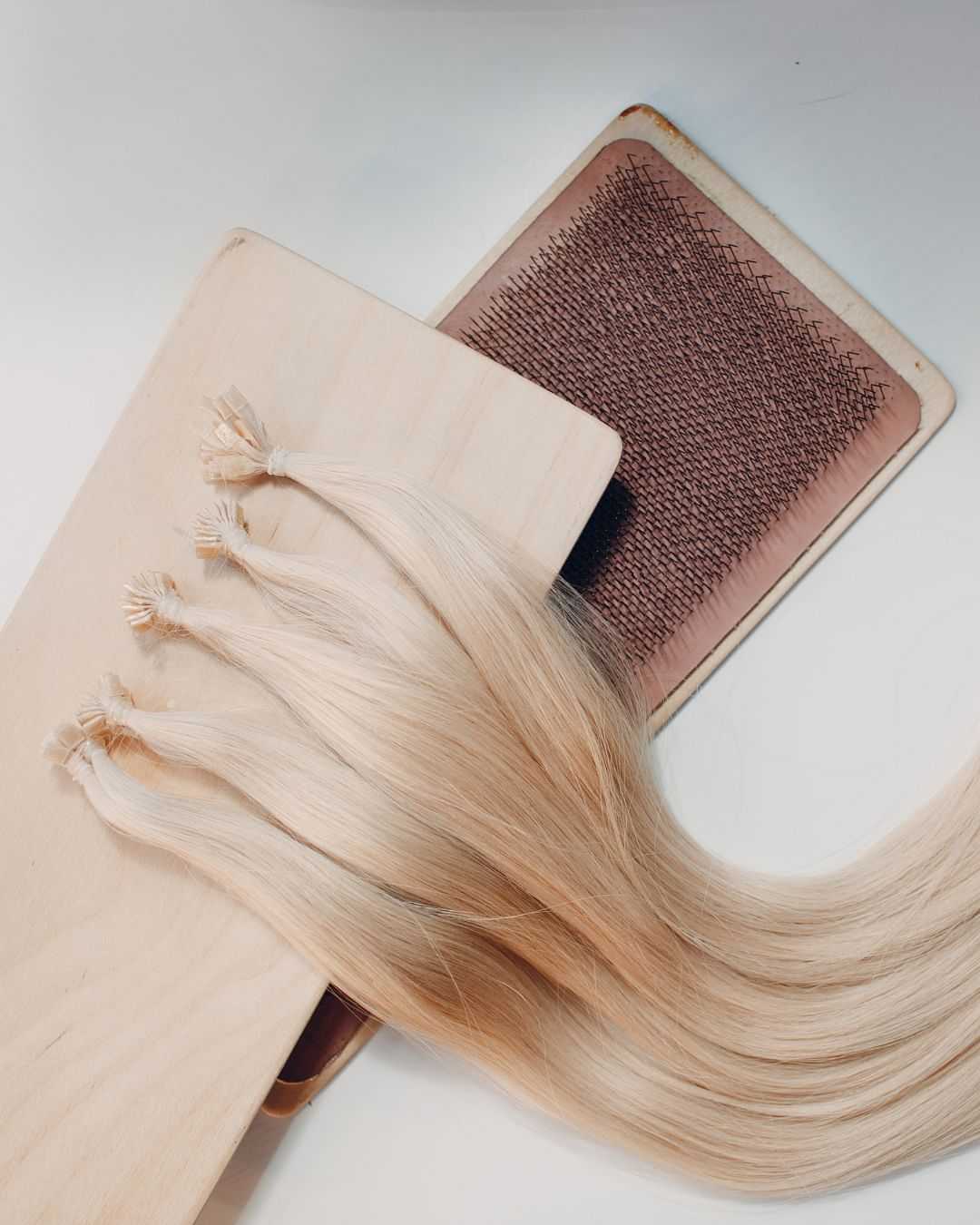Blonde hair extension and a brush on a wooden surface.