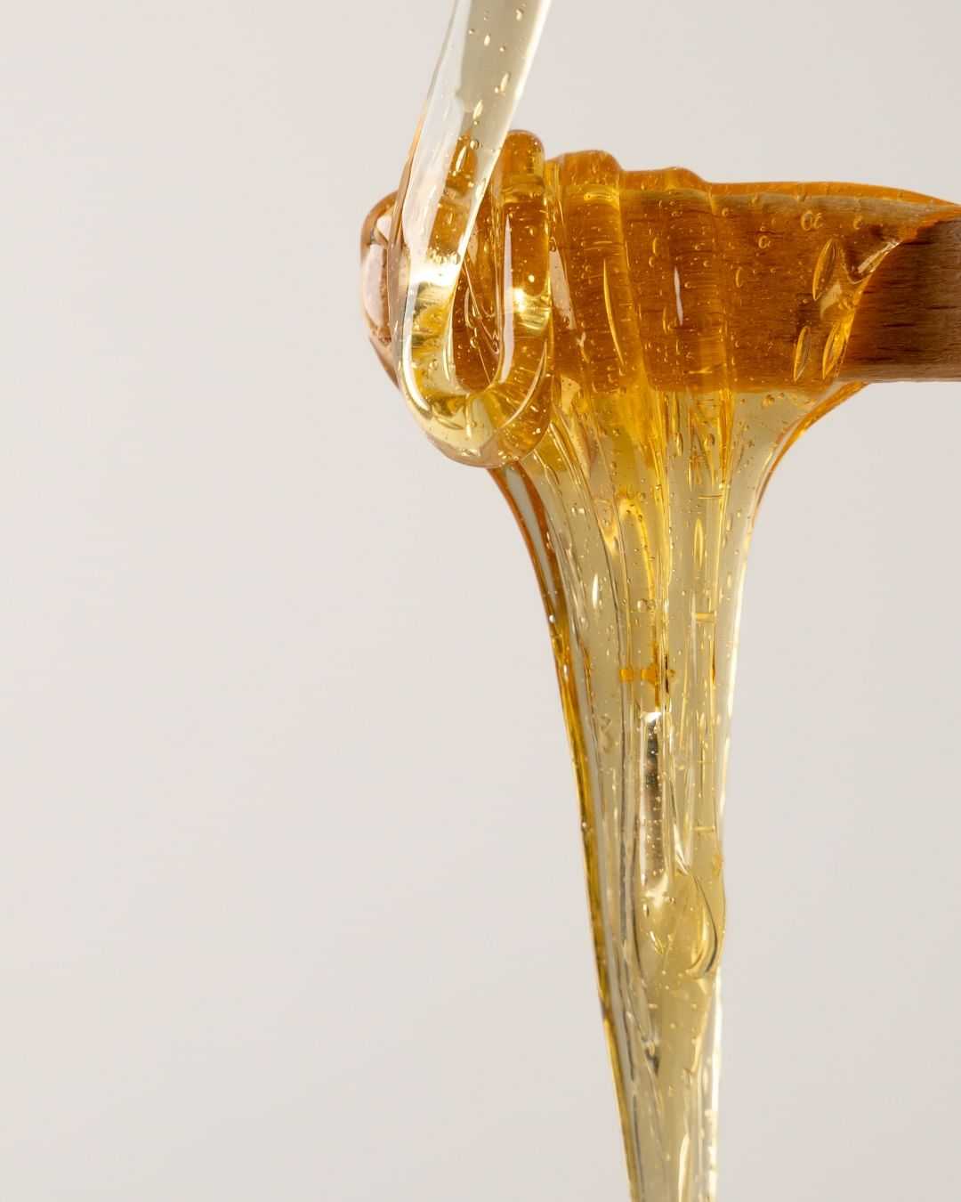 Honey dripping from a wooden dipper against a plain, light-colored background.