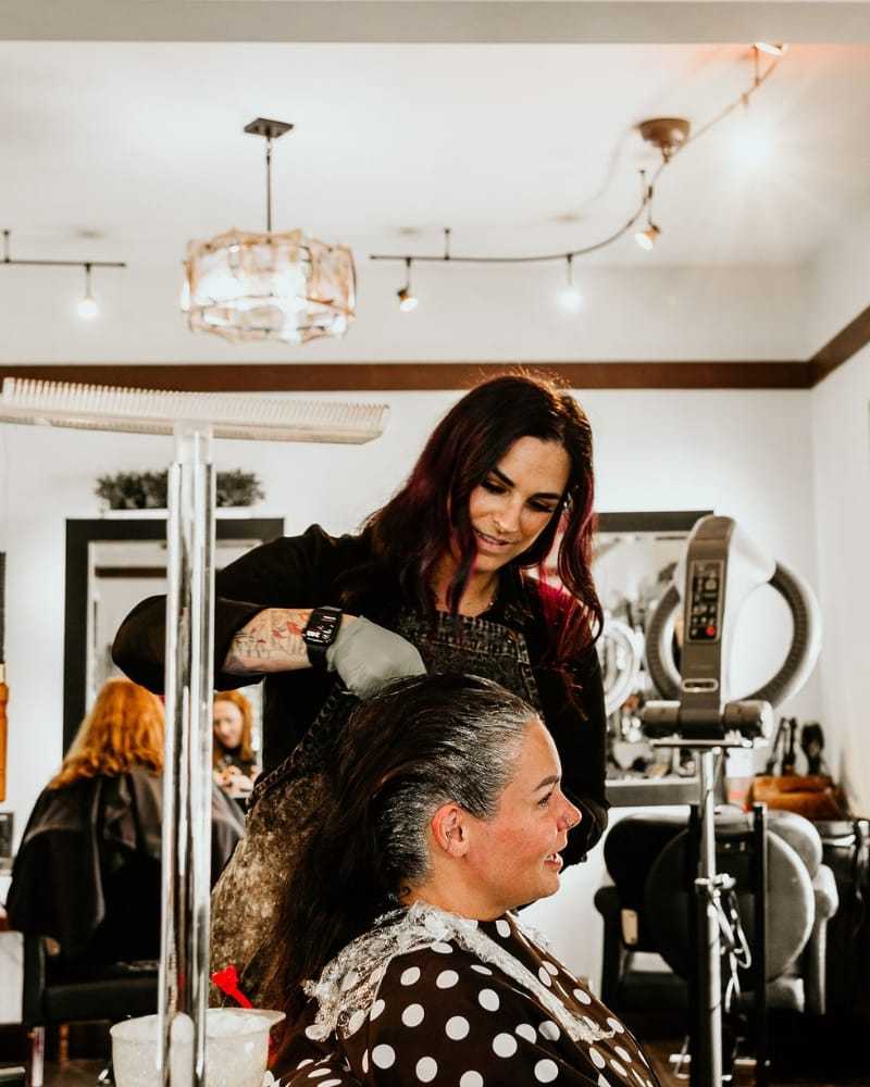 Woman styling another woman's hair in a salon setting.