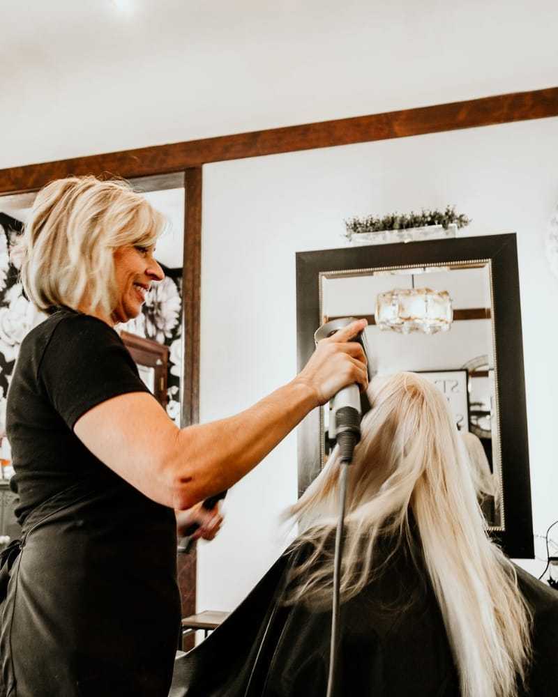 Hairstylist blow-drying long blonde hair in a salon.
