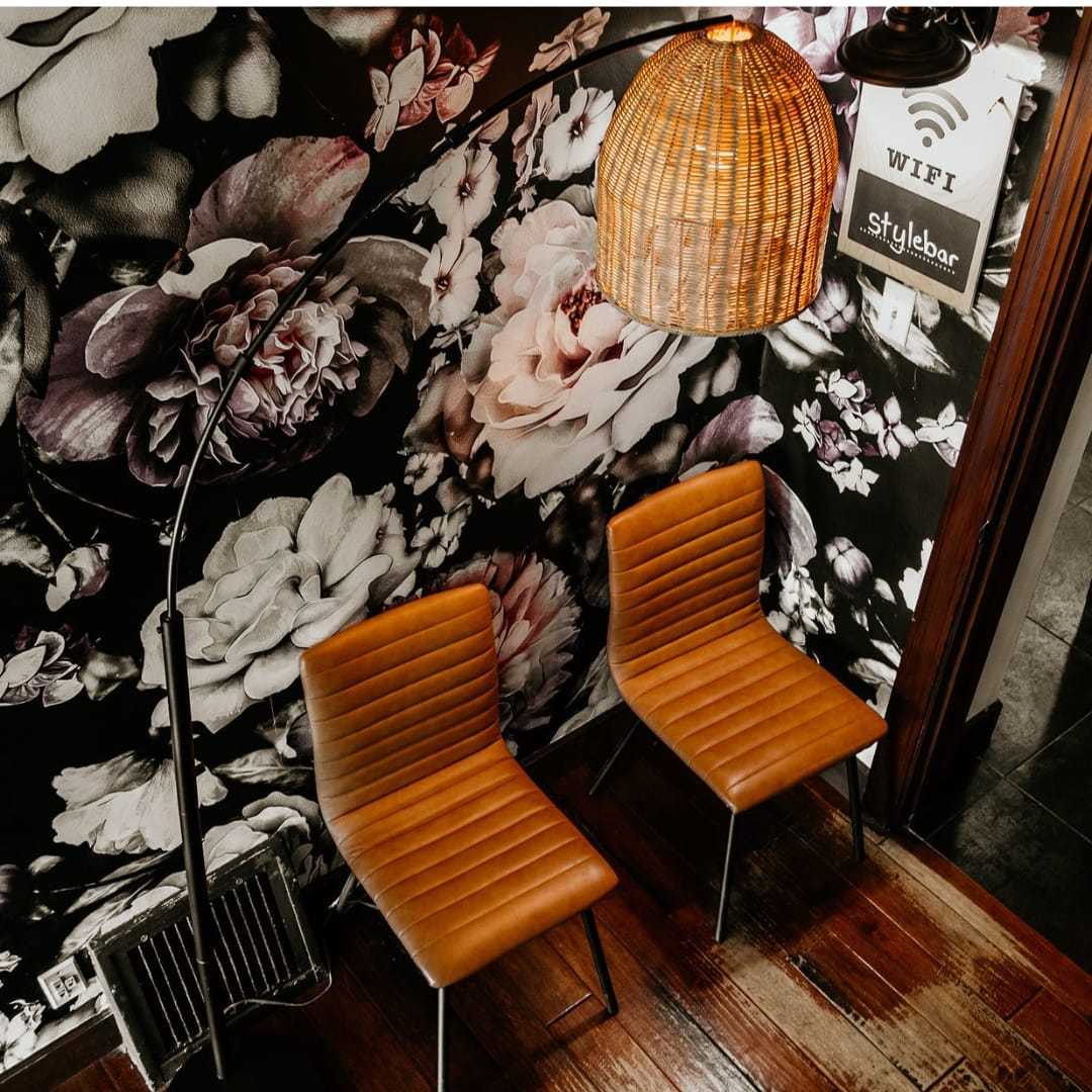 Cozy waiting area with floral wallpaper, two brown chairs, and a wicker lamp. WiFi available.