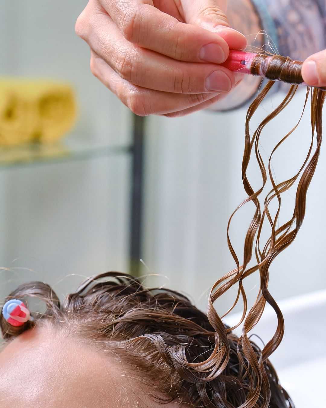 Person having hair curled with pink hair rollers, close-up of hands and curly hair strands.
