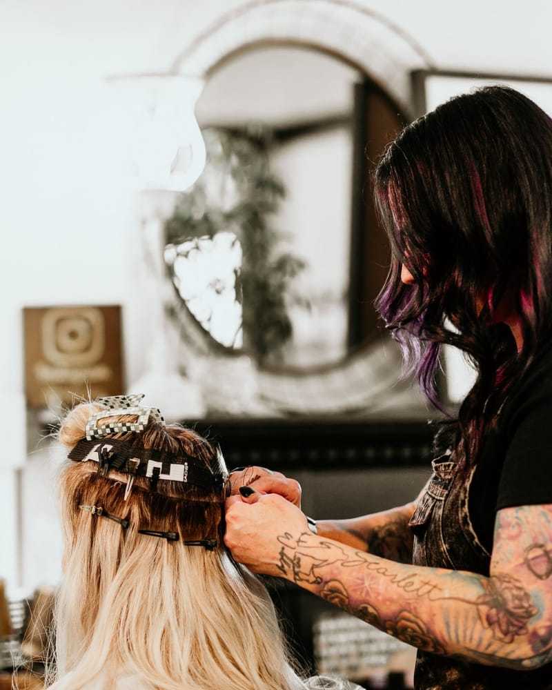 Hair stylist applying extensions to a client's hair in a salon.