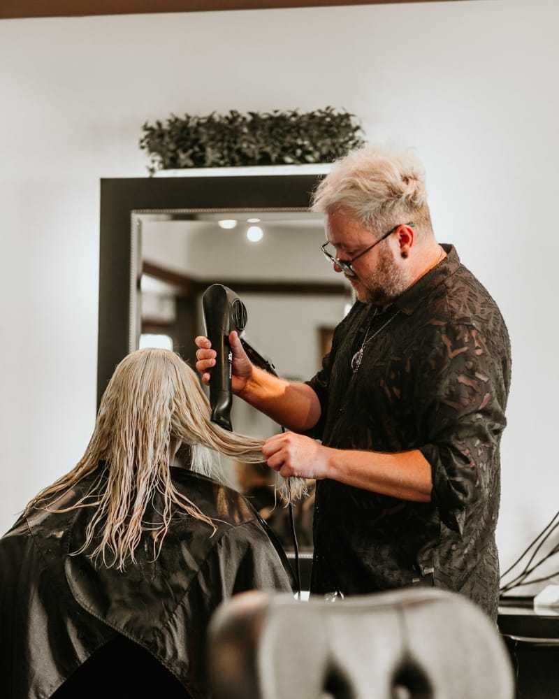 Hairstylist blow-drying a client's wet blonde hair in a modern salon.